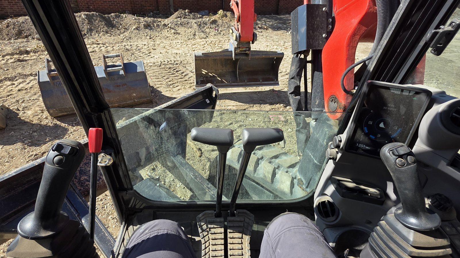 The operator's view from an excavator cab, joysticks and bucket in front